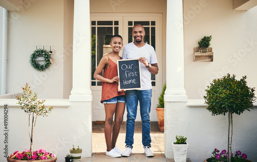 We bought our first house. Portrait of a young couple holding a chalkboard with our first home written on it.