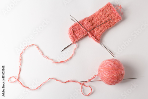 The knitting project is under implementation. A piece of knitting with a ball of yarn and knitting needles on a white background