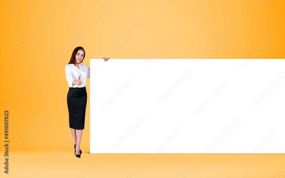 Businesswoman shows thumb up near mockup poster on bright background Businesswoman shows thumb up near mockup poster on bright background