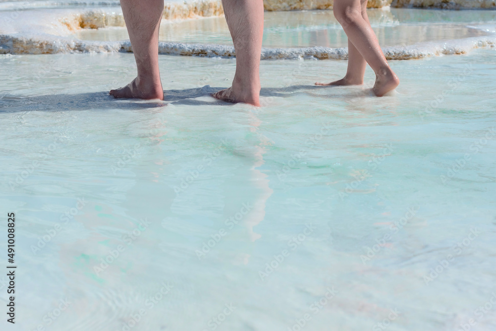 Mans and childs feet standing in thermal water on white limestone terraces. Health and wellness concept. Beauty of nature