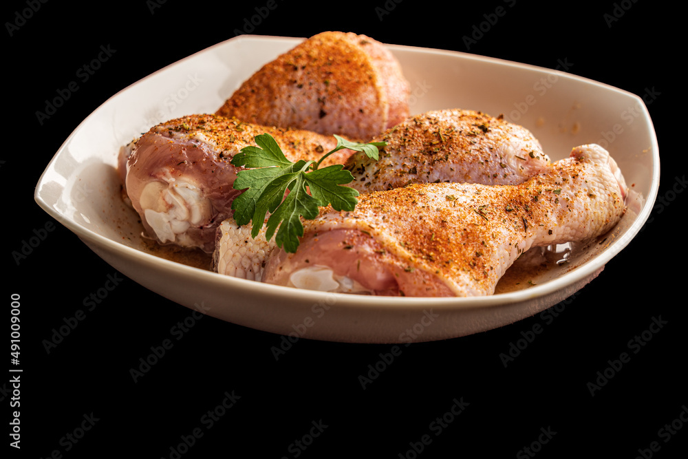 Raw chicken thighs with spices in a plate on a black background.