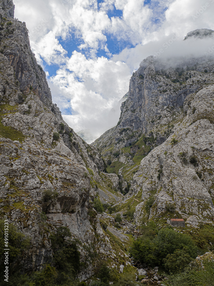 Paisaje de alta montaña con nubes y picos en la ruta del Cares desde Poncebos en Asturias, para senderistas amantes de la naturaleza y excursiones de montaña, en el verano de 2020