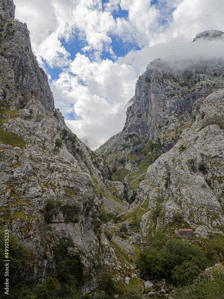 Fototapeta premium Paisaje de alta montaña con nubes y picos en la ruta del Cares desde Poncebos en Asturias, para senderistas amantes de la naturaleza y excursiones de montaña, en el verano de 2020