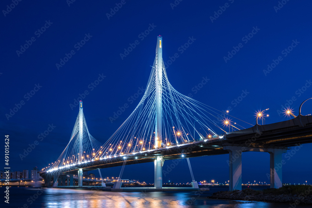 Obraz premium Beautiful landscape of bridge of circle highway road over Neva river near the mouth of it in the blue hour after the sunset. Night view on the buildings of Petersburg city and the Finish gulf