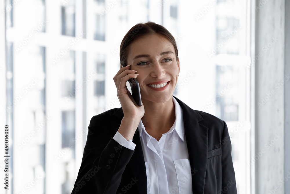 Head shod happy attractive successful millennial female ceo executive manager employee worker holding phone call conversation with colleagues or talking with client, standing near window in office. Head shod happy attractive successful millennial female ceo executive manager employee worker holding phone call conversation with colleagues or talking with client, standing near window in office.