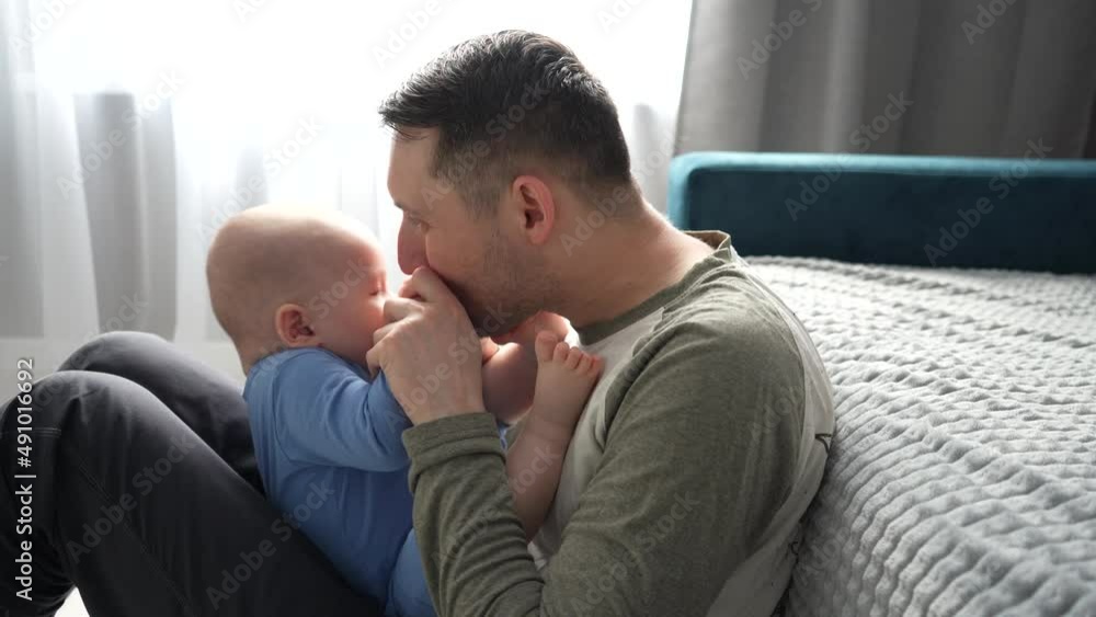 Father plays with a smiling baby son lying on knees at home together. Father plays with a smiling baby son lying on knees at home together.