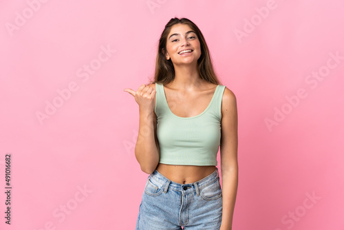 Young caucasian woman isolated on pink background pointing to the side to present a product