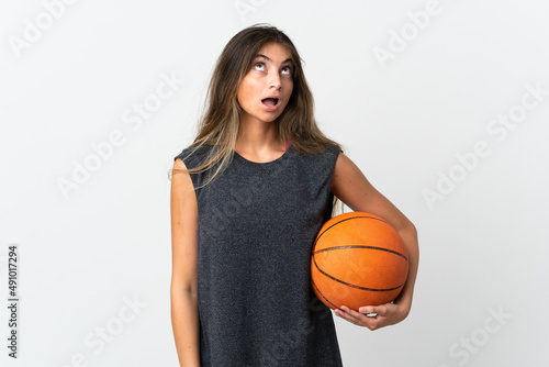 Young woman playing basketball isolated on white background looking up and with surprised expression © luismolinero