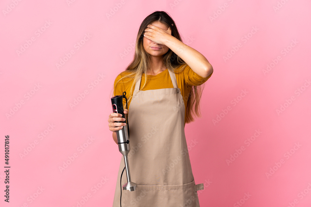 Young chef woman using hand blender isolated on pink background covering eyes by hands. Do not want to see something