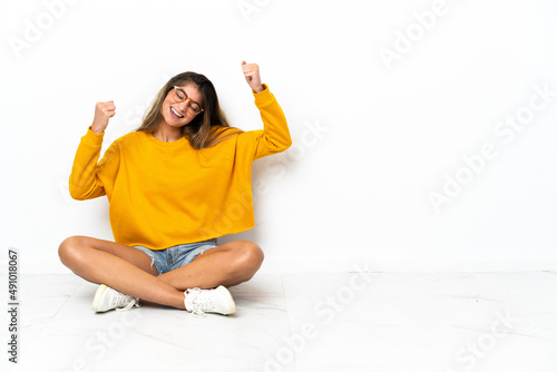Young woman sitting on the floor isolated on white background celebrating a victory