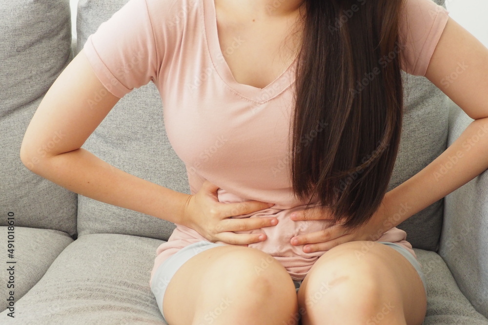 Woman using her hands touching her tummy. Feeling painful after eating something unhygienic or during her menstrual period. Women health and medical treatment concept Woman using her hands touching her tummy. Feeling painful after eating something unhygienic or during her menstrual period. Women health and medical treatment concept