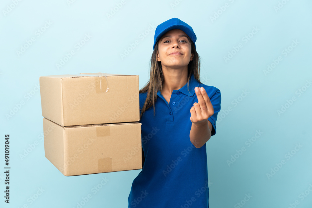 Young delivery woman isolated on blue background making money gesture Young delivery woman isolated on blue background making money gesture