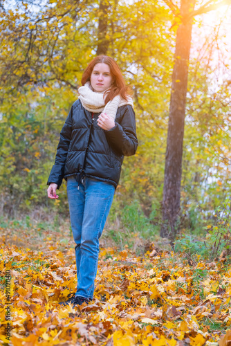 a portrait of a red - haired smiling girl in a jacket and scarf with her hair loose in full growth walks in the park . against the background of autumn nature, the concept of human emotion