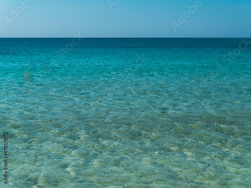 Smooth sea waves blue pattern under crystal clear light blue sky © Dimitrios