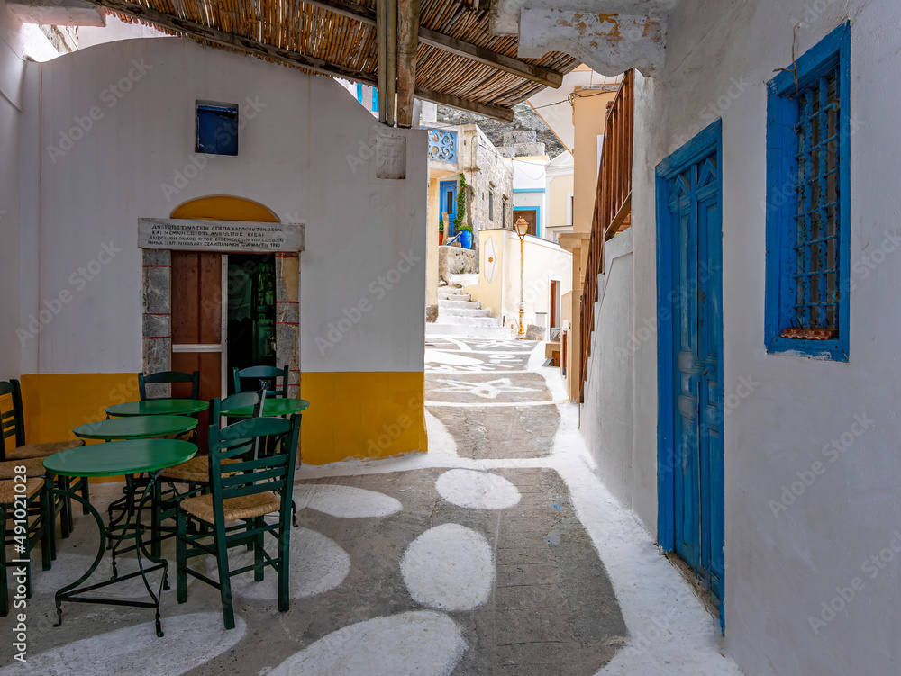 Green chairs and tables in front of a chapel and an alley, Olympos town, Karpathos, Greece. Green chairs and tables in front of a chapel and an alley, Olympos town, Karpathos, Greece.