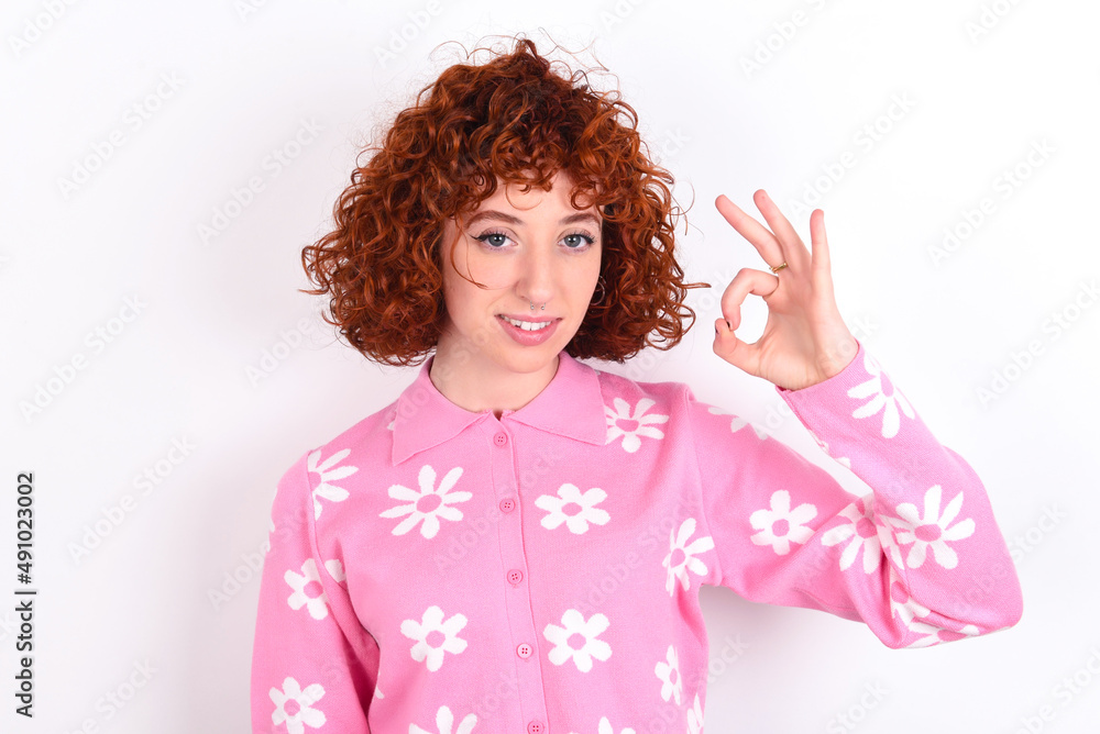 young redhead girl wearing pink floral t-shirt over white background hold hand arm okey symbol toothy approve advising novelty news young redhead girl wearing pink floral t-shirt over white background hold hand arm okey symbol toothy approve advising novelty news