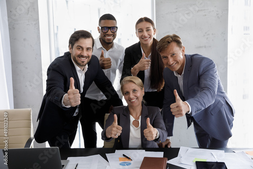 Excited group of happy multiracial different ages business people managers coworkers employees looking at camera, showing thumbs up gestures, proposing offers, satisfied with corporate career. photo