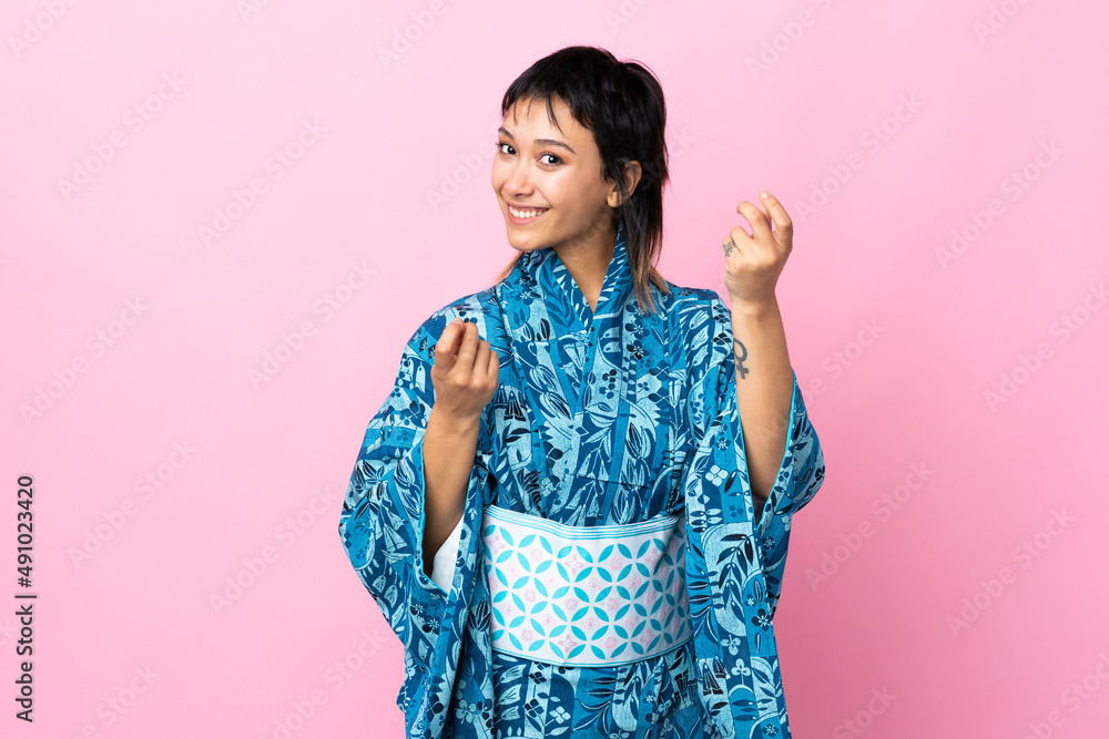 Young woman wearing kimono over isolated blue background making money gesture Young woman wearing kimono over isolated blue background making money gesture
