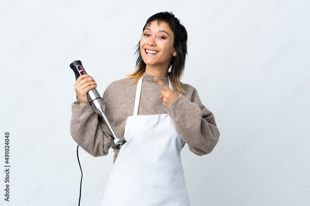Chef Uruguayan girl using hand blender over isolated white background pointing finger to the side Chef Uruguayan girl using hand blender over isolated white background pointing finger to the side