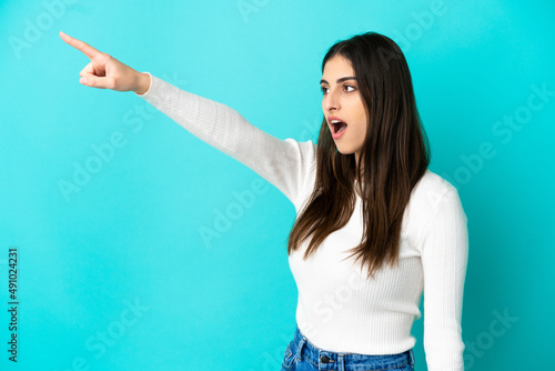 Young caucasian woman isolated on blue background pointing away