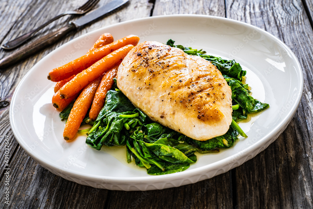 Fried chicken breast with spinach and carrots on wooden table Fried chicken breast with spinach and carrots on wooden table