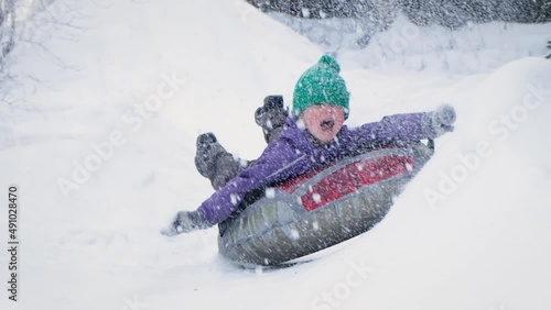 Cute child boy riding on snow tubing rising hands up. Kid sledding slide down hill. Winter fun activity outdoor. photo