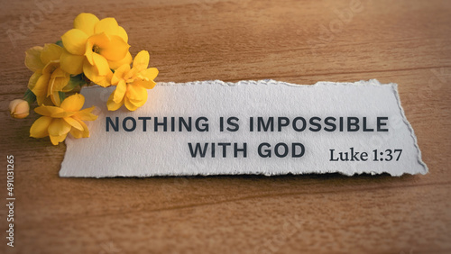 Top view of Bible verse Nothing is impossible with God. Yellow flower and wooden background. photo