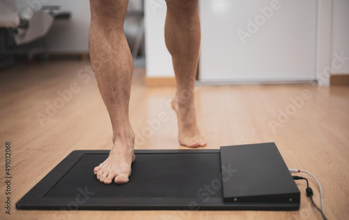 a man in a medical office specialized in posurology with his feet on a platform to analyze the pressure exerted and the biomechanical study of foot drop photo