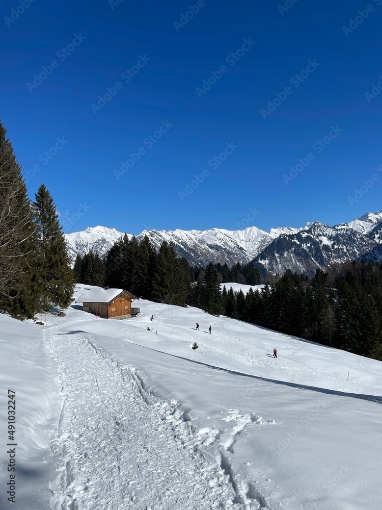 Wanderer laufen an einem sonnigen Wintertag durch den Schnee in Oberstdorf nahe einer Hütte zwischen der Bergstation Söllereck und der weiter entfernten Hütte Hochleite. 