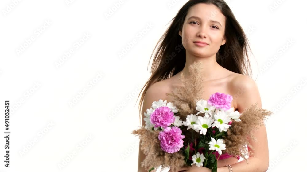 Young pretty lady holding a bouquet of flowers covering her naked breast with hair blowing in the wind over white background. Young pretty lady holding a bouquet of flowers covering her naked breast with hair blowing in the wind over white background.