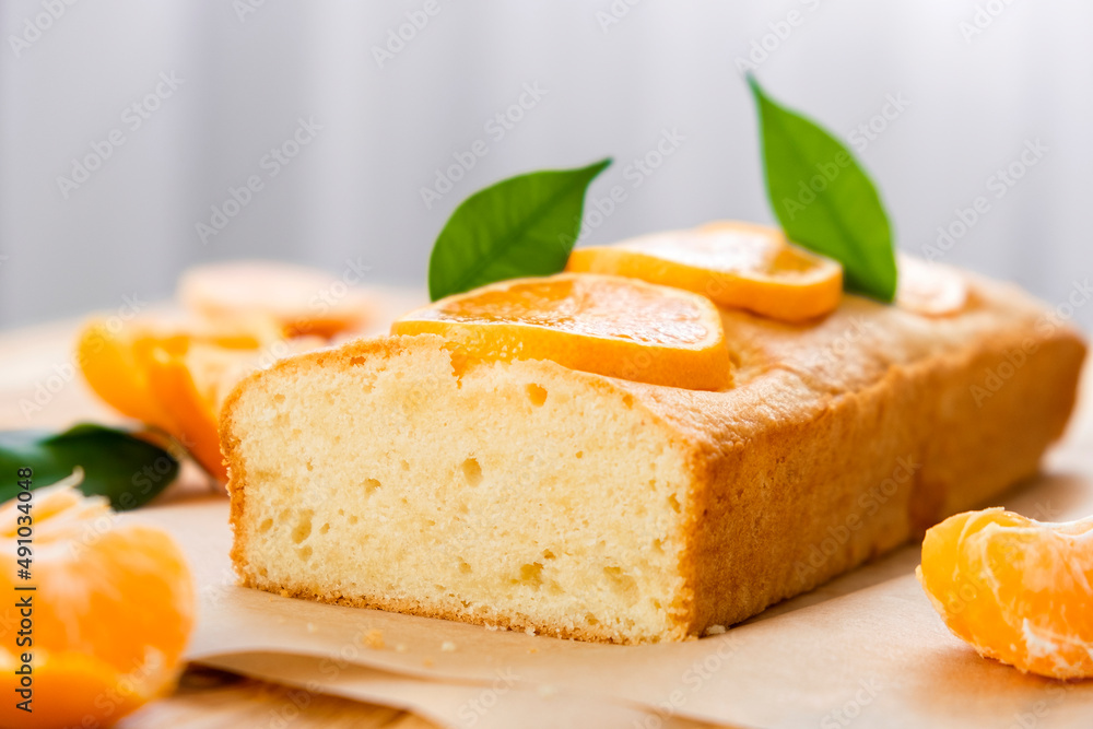 Moist mandarin pound cake on parchment with pieces of fresh tangerine on rustic wooden background. Delicious breakfast, traditional English tea time. Reciepe of citrus pie.