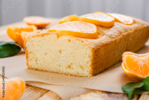 Moist orange fruit pound cake on parchment on rustic wooden background with slices of orange. Delicious breakfast, traditional English tea time. Recipe of orange pie loaf.