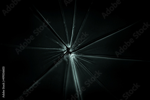 The hole in the broken and cracked glass on black background, closeup