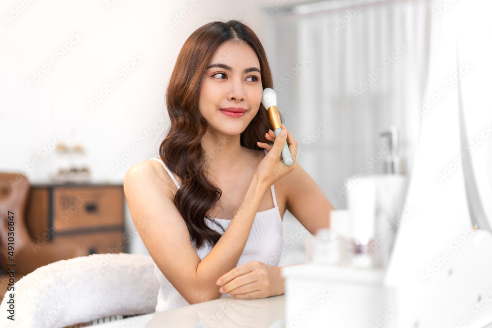 Smiling of young beautiful pretty asian woman clean fresh healthy white skin looking at mirror.asian girl holding make-up brushes and make up on face with cosmetics set at home.facial beauty