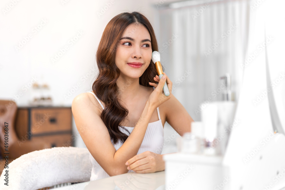 Smiling of young beautiful pretty asian woman clean fresh healthy white skin looking at mirror.asian girl holding make-up brushes and make up on face with cosmetics set at home.facial beauty Smiling of young beautiful pretty asian woman clean fresh healthy white skin looking at mirror.asian girl holding make-up brushes and make up on face with cosmetics set at home.facial beauty