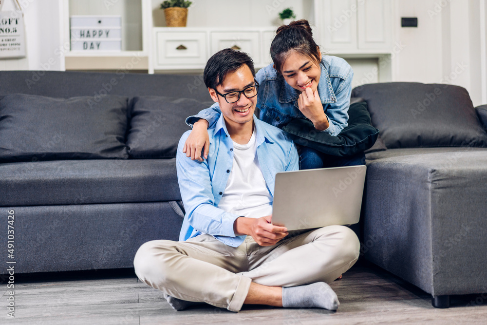 Young asian couple family having good time using technology laptop computer together.Happy couple checking social media and reading news or shopping online while sitting on at home Young asian couple family having good time using technology laptop computer together.Happy couple checking social media and reading news or shopping online while sitting on at home