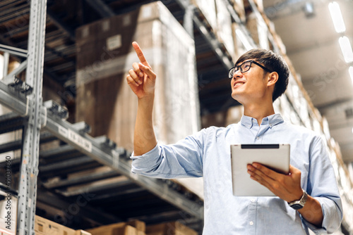 Portrait of smiling asian engineer foreman man order details checking goods on tablet and supplies on shelves with goods background in warehouse.logistic and business export