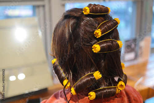 The back of a woman rolling her hair using beauty tools.