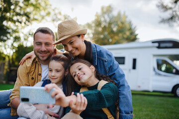 Happy young family with two children ltaking selfie with caravan at background outdoors.