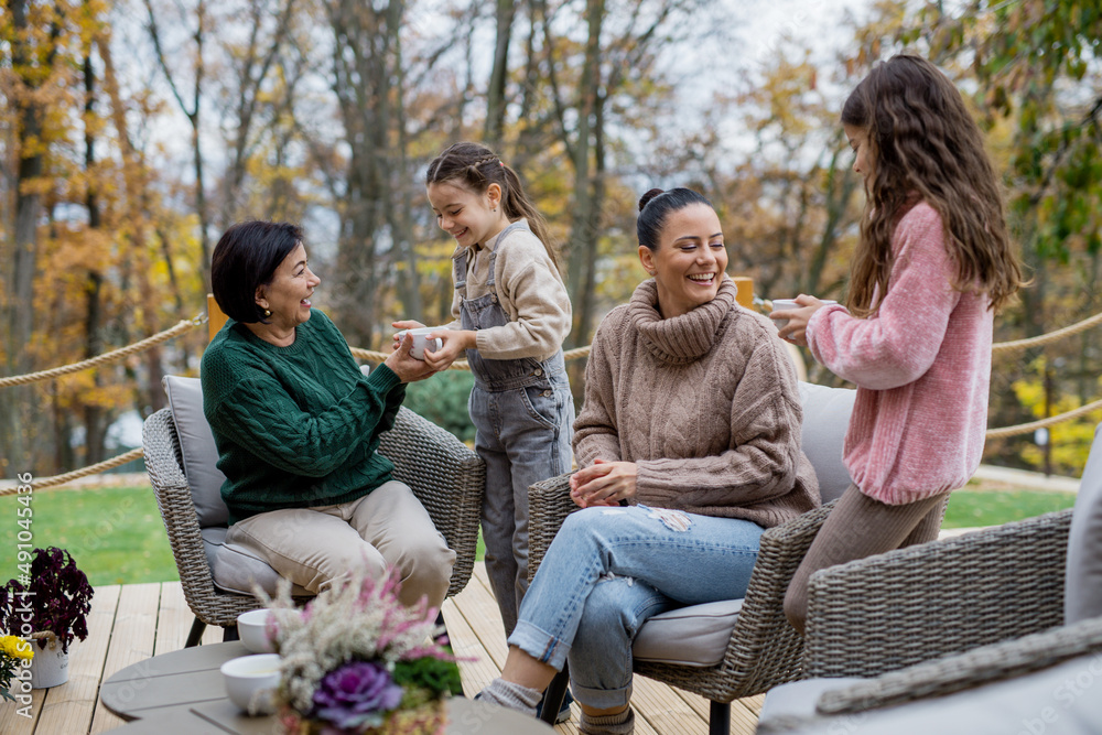 Two happy sisters with mother and grandmother sitting and drinking tea outdoors in patio in autumn. Two happy sisters with mother and grandmother sitting and drinking tea outdoors in patio in autumn.