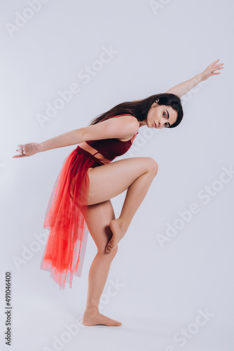 portrait of a beautiful ballerina in a red dress on a white background. The girl shows the movement of the dance. dressed in a red outfit