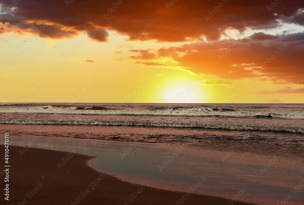 Waves at sea on sunset. Waves at sea during storm and wind. Wave from the sea goes on land to the beach. Splashing Waves in ocean on sunrise background, texture. Wave at Rising Storm at coastline.