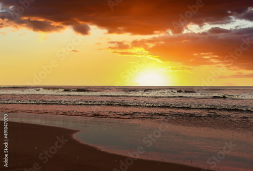 Waves at sea on sunset. Waves at sea during storm and wind. Wave from the sea goes on land to the beach. Splashing Waves in ocean on sunrise background, texture. Wave at Rising Storm at coastline.