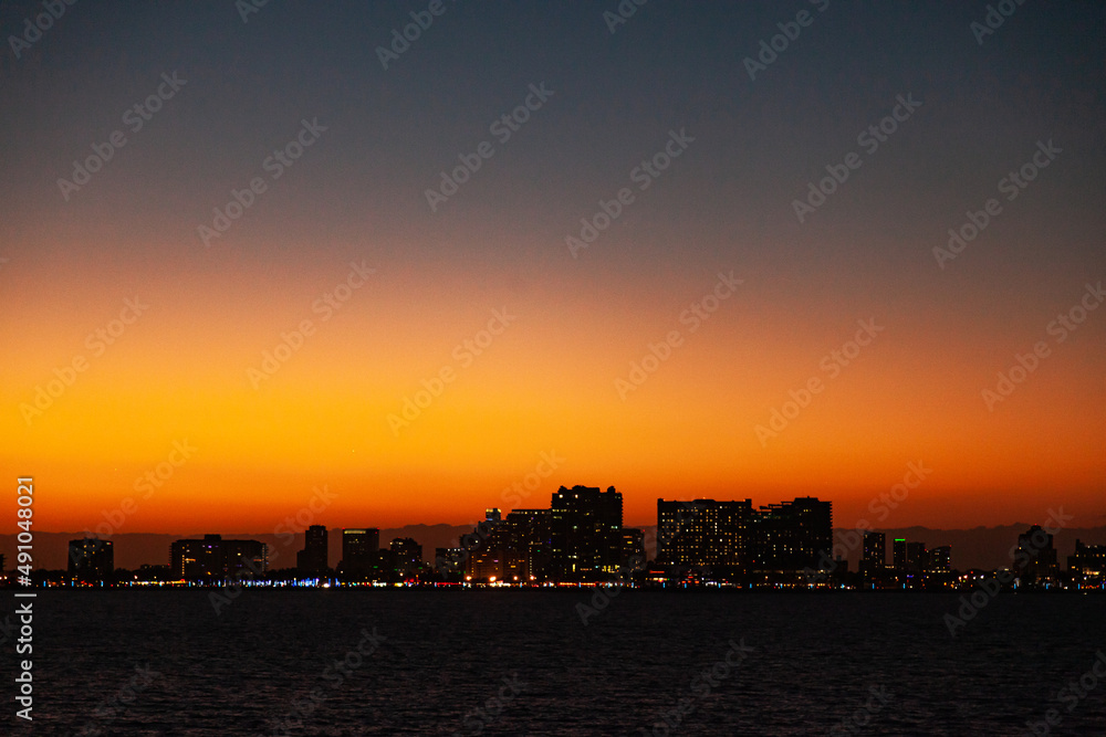 Night city of Fort Lauderdale on the coast of the Atlantic Ocean, against the backdrop of twilight with an orange sky.