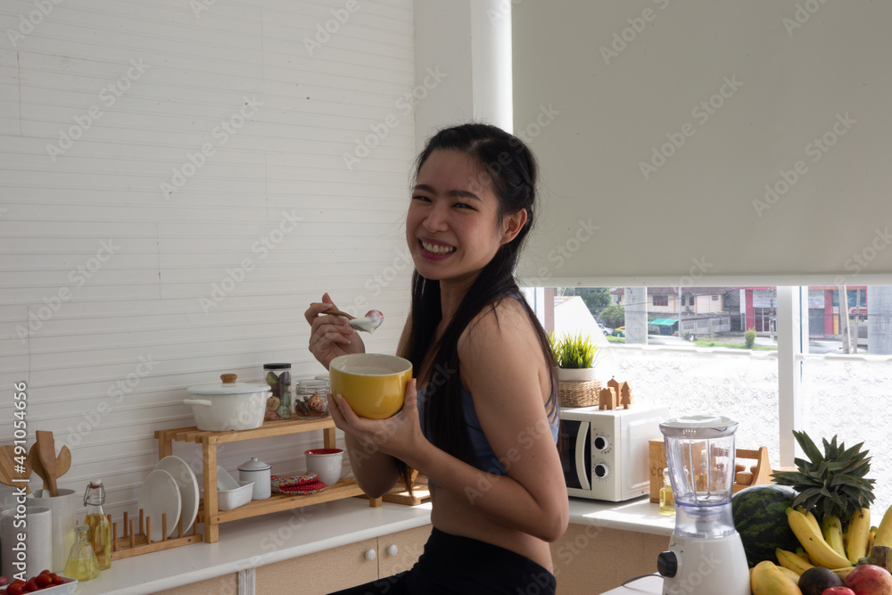 young Asian woman cooking vegetable healthy food and eating or drinking in home kitchen