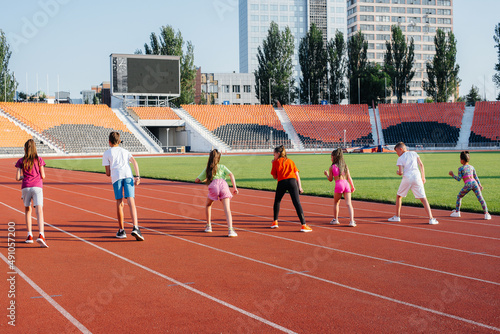 A large group of children, boys and girls, run and play sports at the stadium during sunset. A healthy lifestyle.