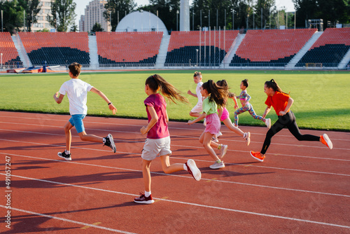 A large group of children, boys and girls, run and play sports at the stadium during sunset. A healthy lifestyle. © Andrii