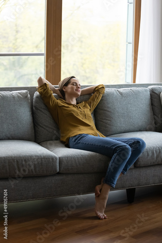 Vertical view serene woman relax on sofa with eyes closed and hands behind head enjoy carefree day off, breath fresh air, climate control inside for comfort living. Tenant, modern smart house concept © fizkes