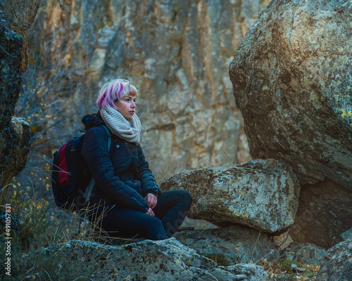 Tranquilidad en la naturaleza, chica joven sentada en medio de la naturaleza, mujer con pelo rosa y mochila sentada entre rocas photo