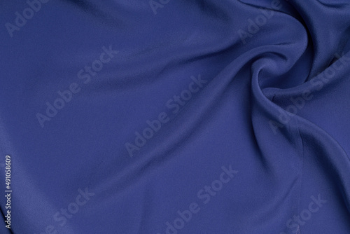 Blue abstract background. Dark blue silk satin texture background. Shiny fabric with wavy soft pleats. Dark blue elegant background with copy space for your design